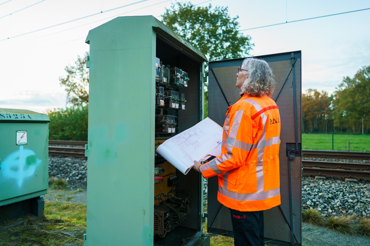 Inspecteur Seinwezen Franka inspecteert een elektriciteitskast naast het spoor.