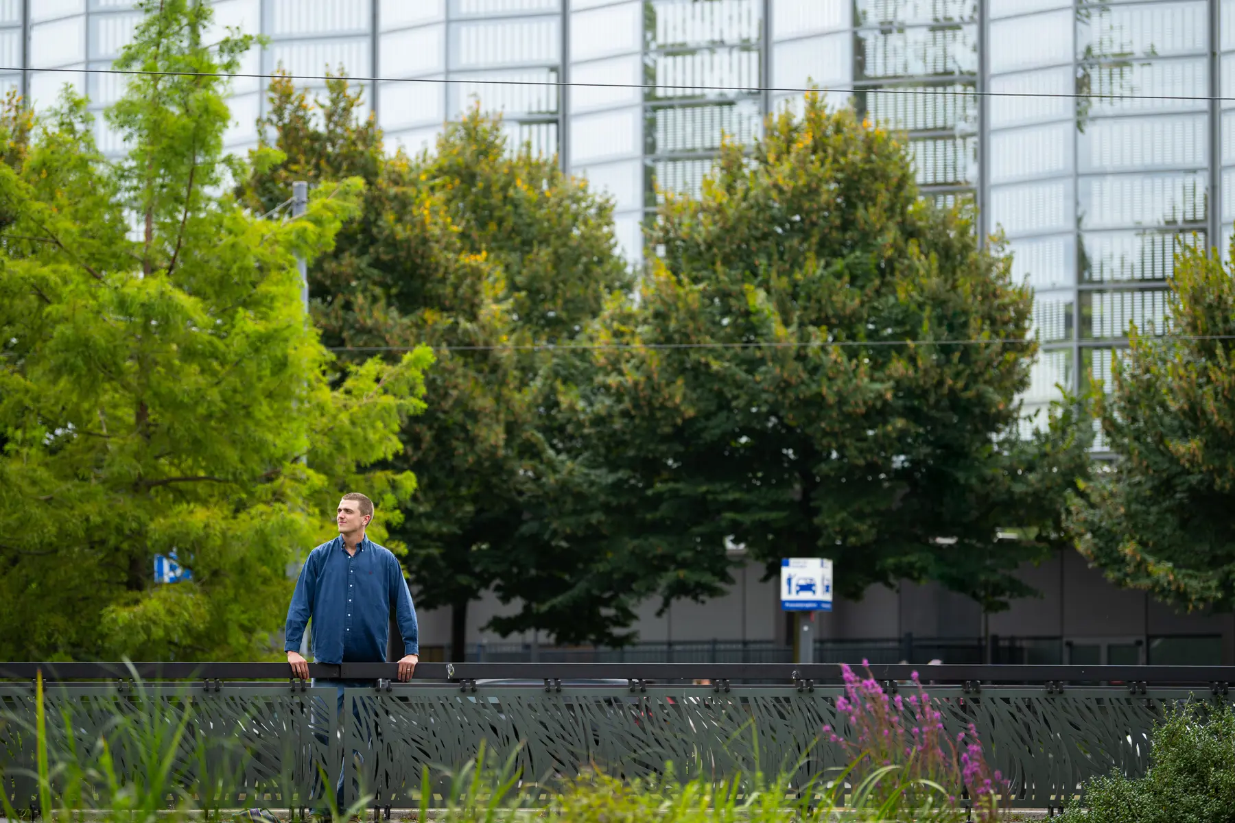Bastiaan staat op een brug, middenin allemaal groen. Zoals bomen, planten, struiken.