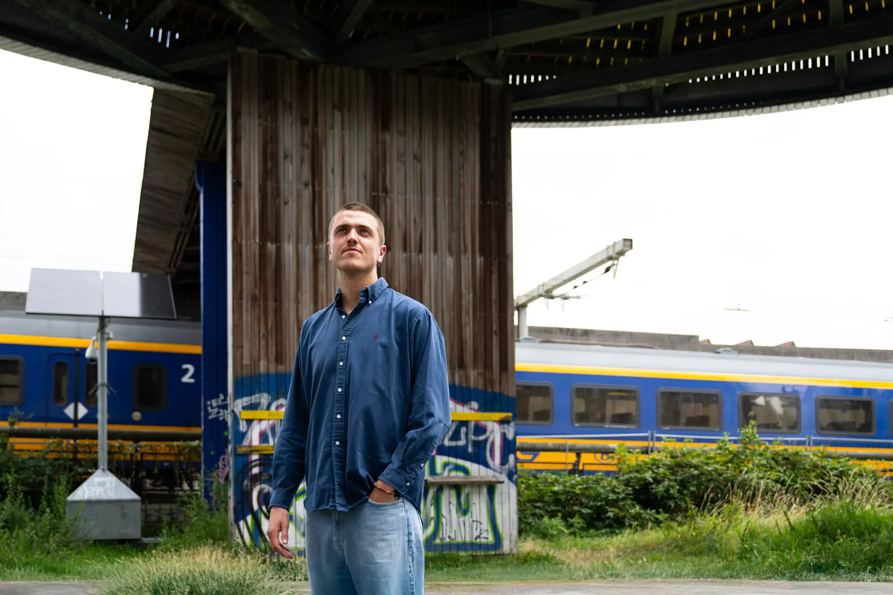 Bastiaan staat onder een soort koepel. Achter hem rijdt een trein. Hij kijkt schuin omhoog.