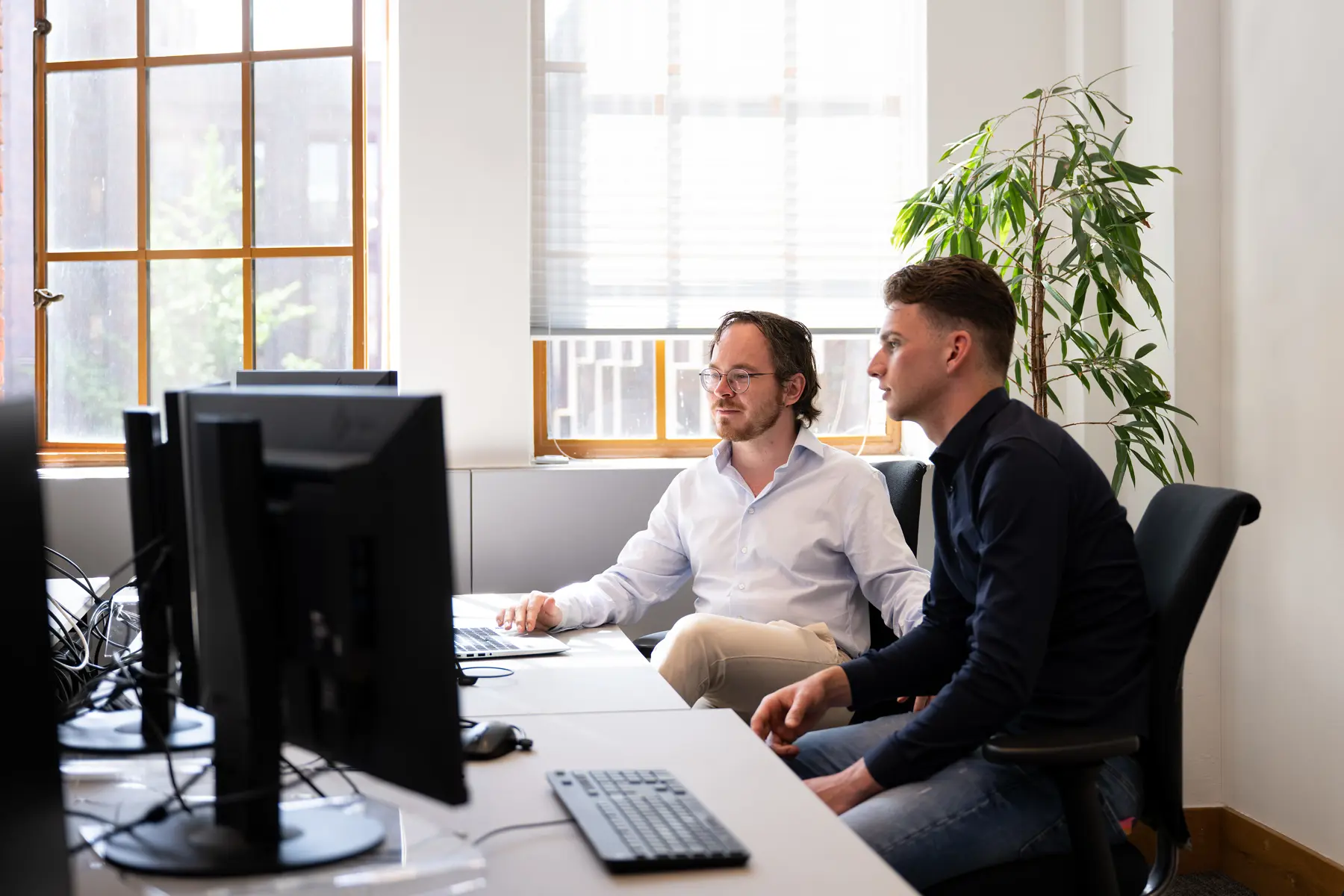 Ruben en Mark zitten samen achter het bureau, kijkend naar computerschermen. Ze zitten in een kamer op de Inktpot van ProRail. 