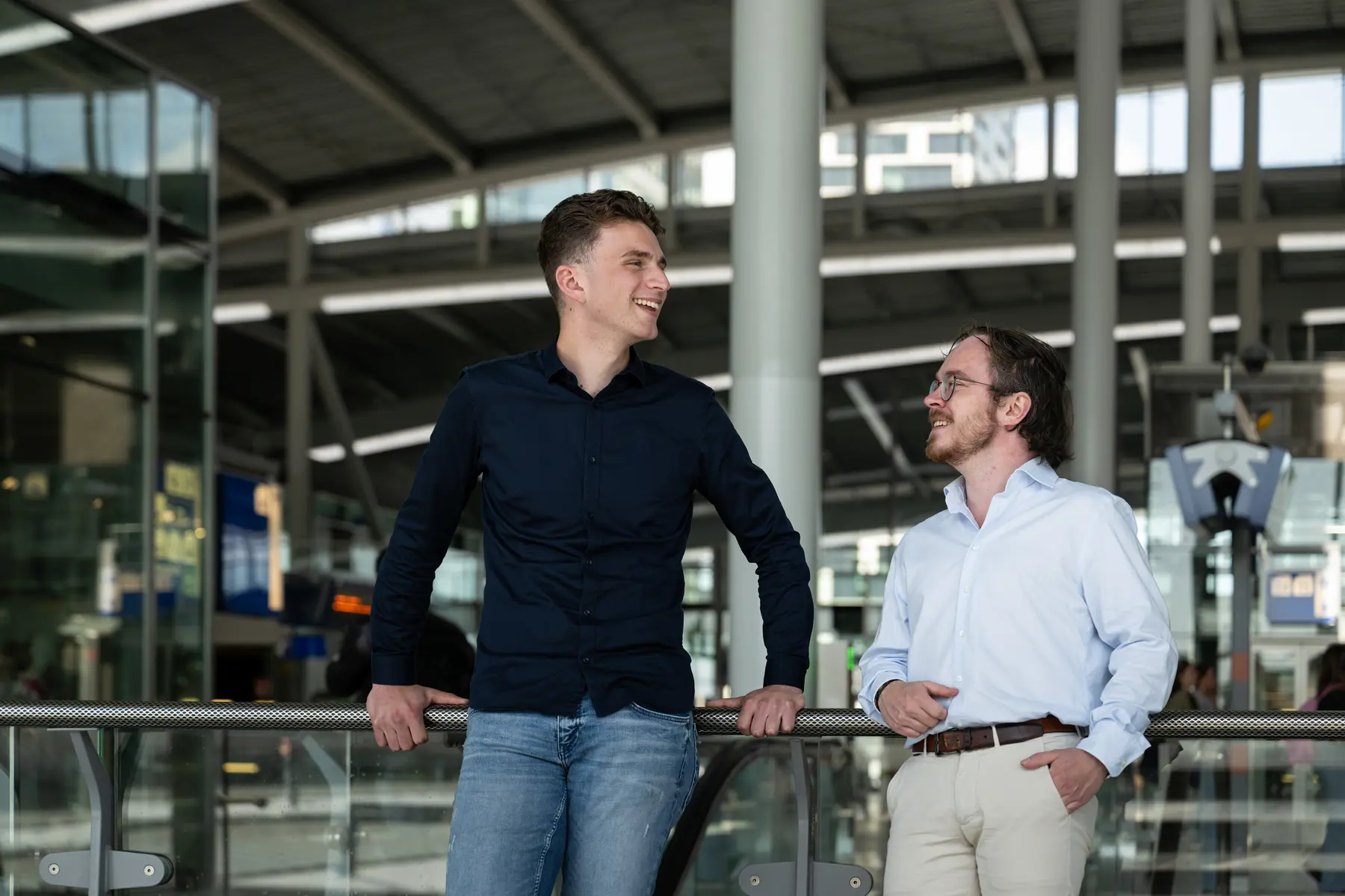 Ruben en Mark staan op Utrecht Centraal. Ze kijken naar elkaar en lachen.