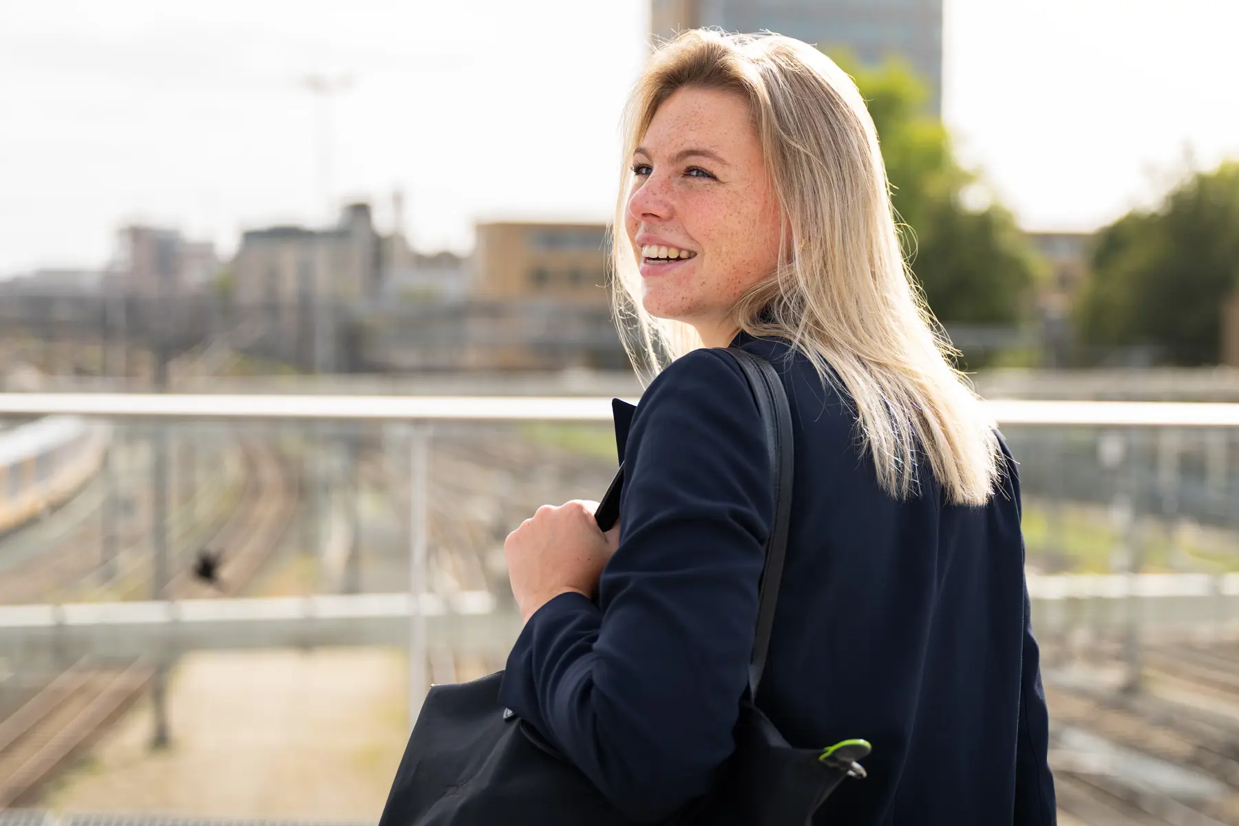 Merel Winters, technisch trainee, staat op de loopbrug over het spoor van Utrecht Centraal. Ze lacht en heeft haar hoofd richting de camera, maar kijkt er net langs. 