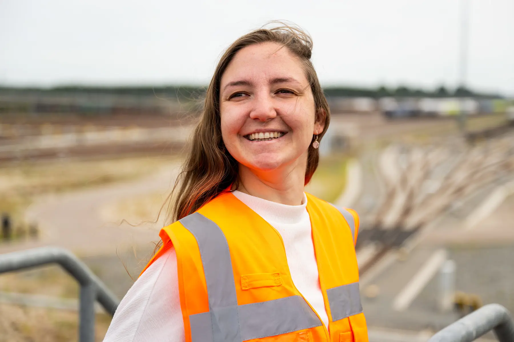 Micha van Os heeft een oranje hesje aan en lacht. Ze staat op een verhoging, waardoor achter haar het goederenemplacement Kijfhoek ligt. 